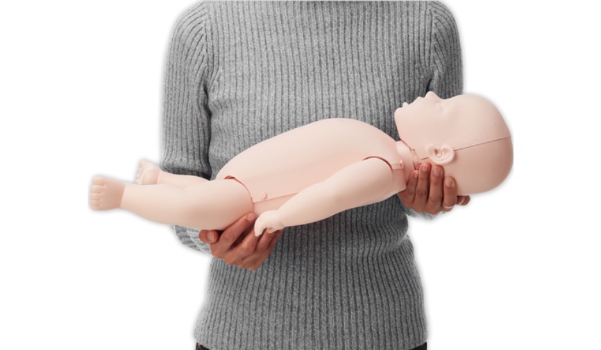 Woman in grey long sleeved shirt holding Brayden Baby CPR Manikin