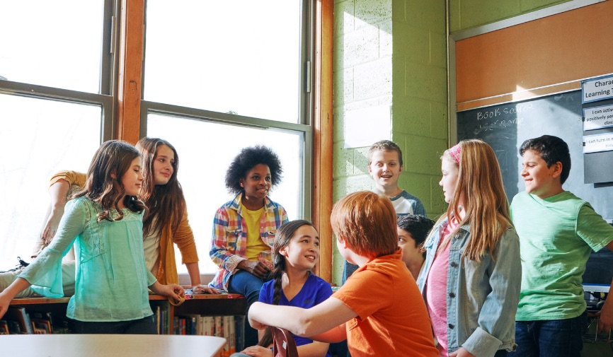 Group of 9 diverse pre-teen aged students talking in a classroom