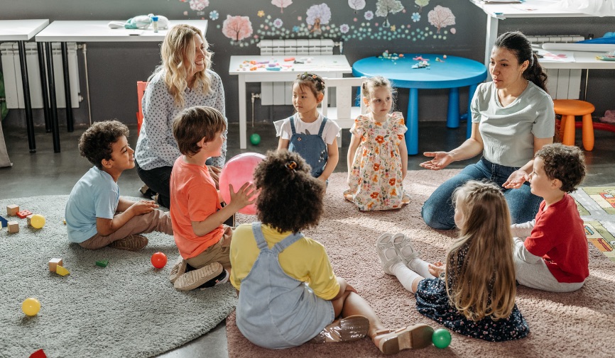 young children sitting down in a circle, classroom setting with two teachers