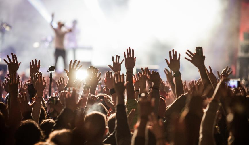 Defibrillator checklist for events A large crowd at an outdoor concert or festival with hands raised in the air, silhouetted against bright stage lighting.