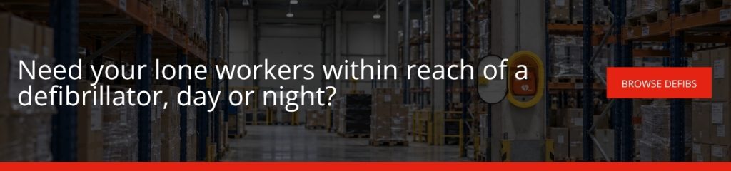 Need your lone workers within reach of a defibrillator day or night: A banner advertisement with a darkened warehouse aisle background showing a wall-mounted defibrillator, with white text reading "Need your lone workers within reach of a defibrillator, day or night?" and a red "Browse Defibs" button.